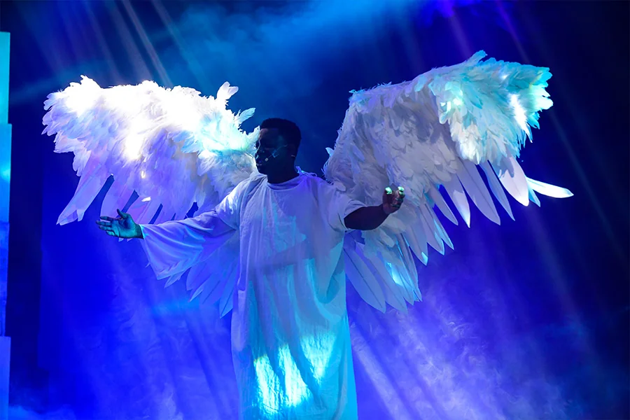 An angel performer with feathered wings under blue stage lights